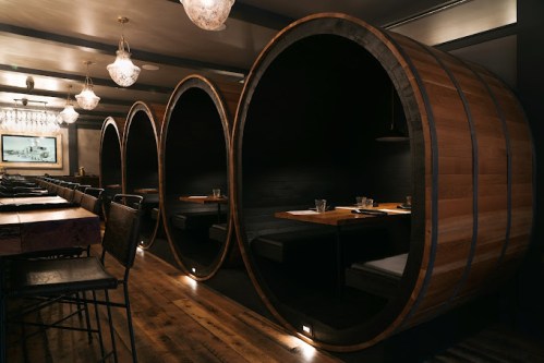 Cozy restaurant interior featuring wooden barrel-shaped booths with dim lighting and elegant decor.