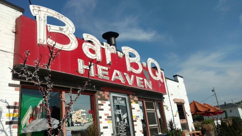 A vibrant BBQ restaurant with a red sign reading "Bar-B-Q Heaven" against a clear blue sky.