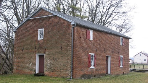 A two-story brick house with red shutters, surrounded by trees and grass, on a cloudy day.