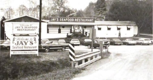 Black and white photo of Jay's Seafood Restaurant, featuring a sign and parked cars in front of the building.