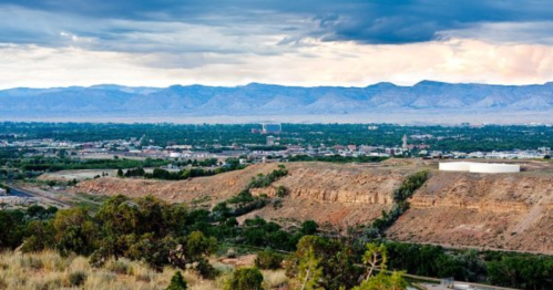 A panoramic view of a valley with mountains in the background, under a cloudy sky. Green hills in the foreground.