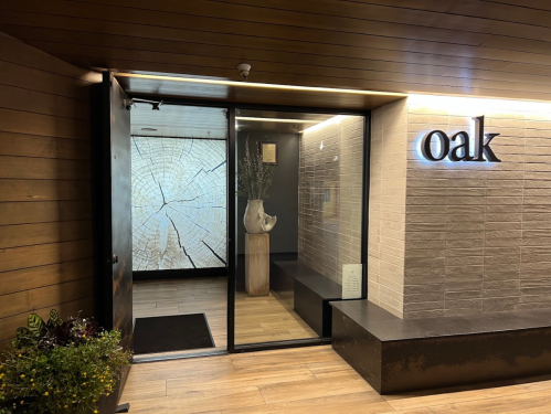 Entrance to a modern restaurant named "oak," featuring a glass door and a decorative wall with a tree ring design.