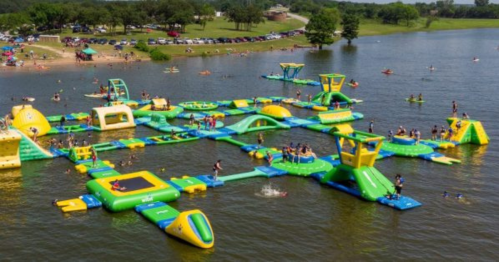 Aerial view of a colorful inflatable water park with people enjoying various activities on a lake.