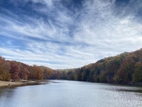 A serene lake surrounded by autumn foliage and a blue sky with wispy clouds.