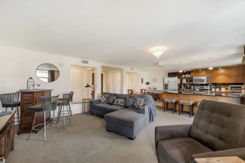 Spacious living area with a gray sectional sofa, bar seating, and a modern kitchen in the background. Bright and inviting.