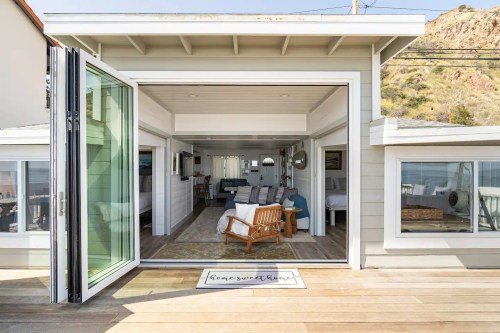 A modern beach house with open doors, showcasing a cozy interior and ocean views.