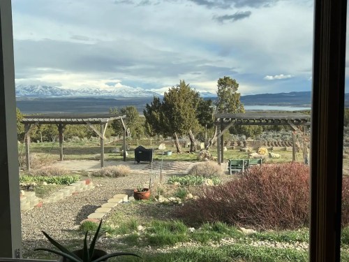 A scenic view of a garden with pergolas, mountains in the background, and a cloudy sky over a vast landscape.