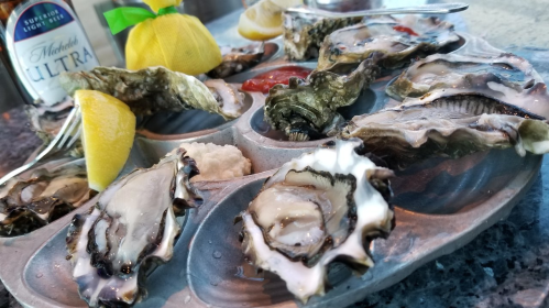 A platter of fresh oysters on ice, garnished with lemon wedges and cocktail sauce.