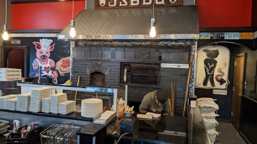 Interior of a BBQ restaurant featuring a grill, stacked plates, and colorful murals of animals on the walls.