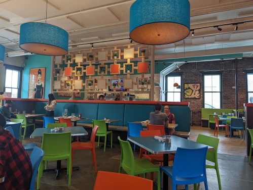Brightly colored restaurant interior with blue and orange lamps, colorful tables, and patrons dining. Art on the walls.