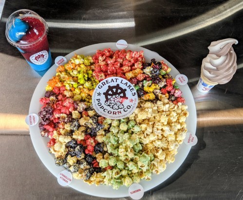 A colorful platter of assorted popcorn flavors from Great Lakes Popcorn Co., with a slushy drink and soft serve ice cream.