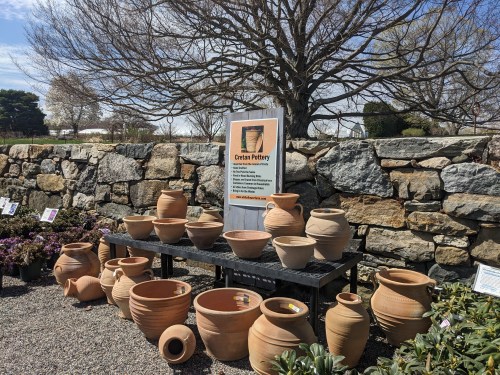 Display of various Cretan pottery pieces on a table in front of a stone wall, with a sign explaining their significance.