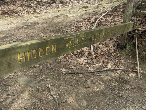 Wooden sign reading "Hidden Valley Reservation" on a dirt path surrounded by leaves and trees.