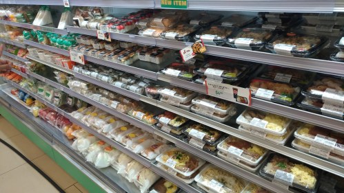 A display of various packaged meals and snacks in a grocery store refrigerator section.
