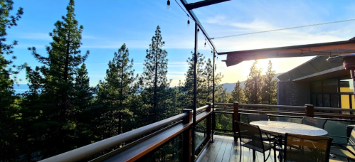 A scenic view from a balcony overlooking tall pine trees and a clear blue sky at sunset.