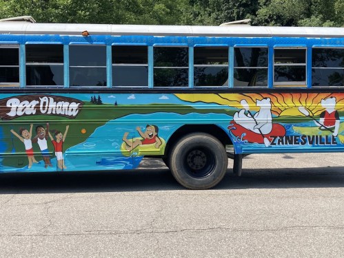 Colorful mural on a bus featuring beach scenes, children playing, and the text "Zanesville" and "Pee Ohana."