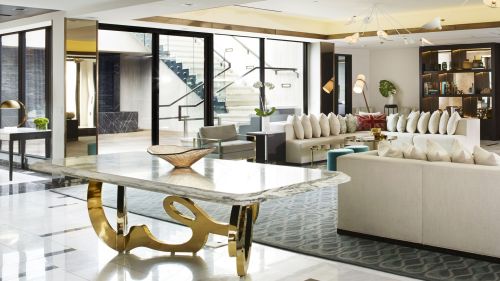Modern lobby with elegant furniture, a marble table, and large windows, featuring stylish decor and a welcoming atmosphere.