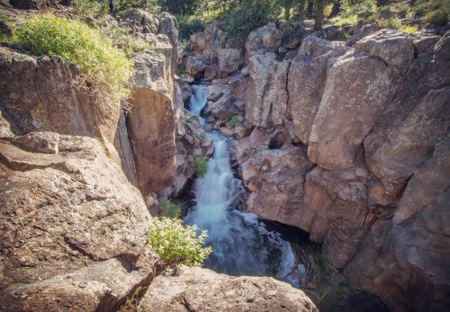 A serene waterfall cascades through rocky cliffs, surrounded by lush greenery and natural beauty.