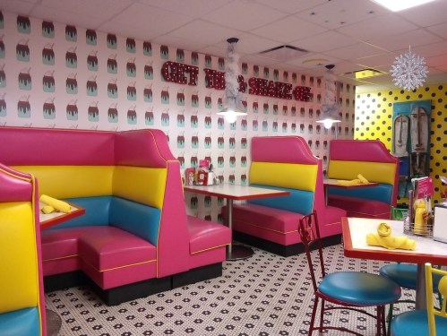 Colorful diner interior featuring pink and yellow booths, patterned walls, and retro decor.
