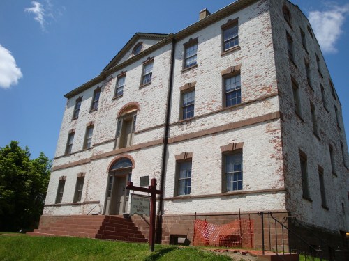 Historic brick building with a white facade, featuring large windows and a sign in front, set against a blue sky.