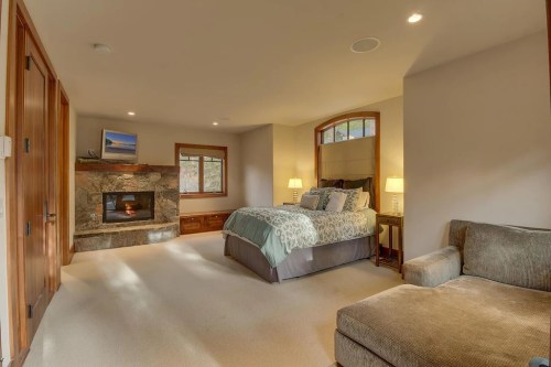 Cozy bedroom with a fireplace, large bed, and a seating area, featuring natural light and warm wood accents.