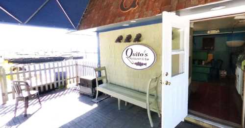 Entrance to Quito's Restaurant & Bar, featuring a sign, bench, and outdoor seating area with a view.