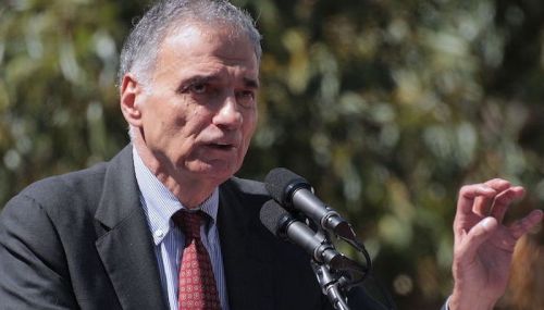 A man in a suit speaks passionately at a podium with microphones, gesturing with his hand.