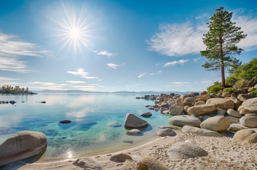 A serene lakeside scene with clear water, smooth rocks, a sandy beach, and a sunlit sky.