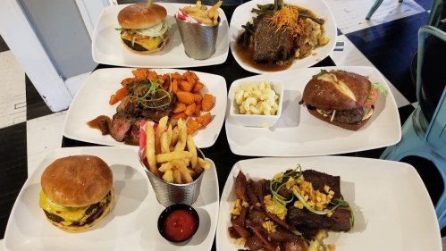 A spread of delicious dishes including burgers, steak, sweet potatoes, fries, and macaroni on white plates.