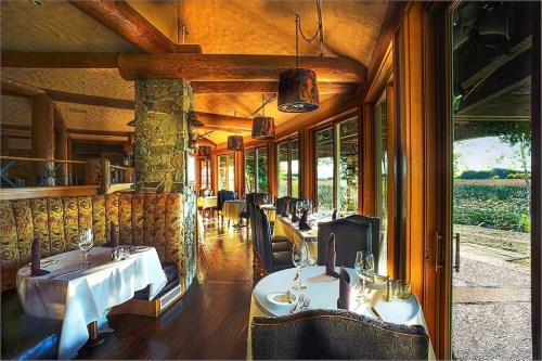 Elegant restaurant interior with wooden beams, cozy seating, and large windows overlooking a scenic view.