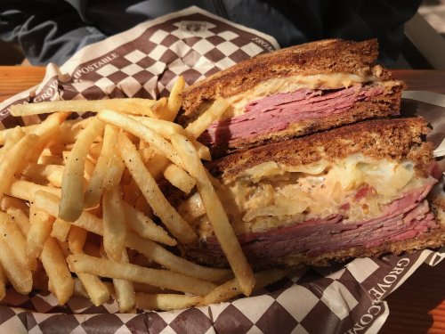 A sliced sandwich with layers of meat and cheese, served with a side of crispy French fries on a checkered paper.