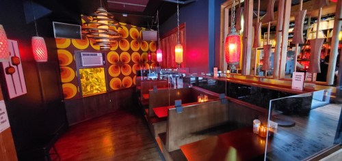 A cozy restaurant interior with colorful decor, red pendant lights, and wooden booths, creating a warm atmosphere.