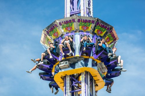 A group of thrill-seekers on a tall amusement park ride, suspended high against a clear blue sky.