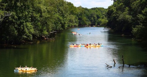 A serene river scene with kayakers and canoers surrounded by lush greenery under a clear blue sky.