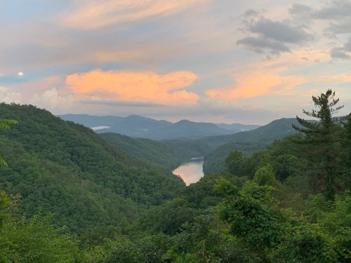 A serene landscape featuring a river winding through lush green mountains under a colorful sunset sky.