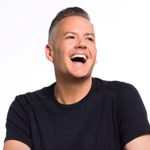 A smiling man with short hair, wearing a black shirt, against a white background. He appears joyful and relaxed.