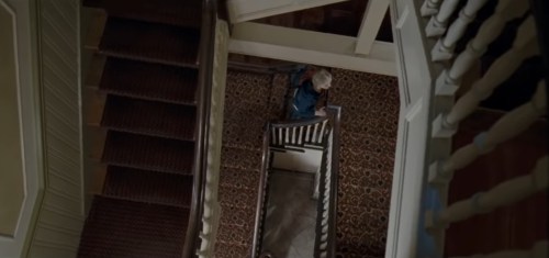 Aerial view of a staircase with a patterned carpet, showing a person standing on the lower level.