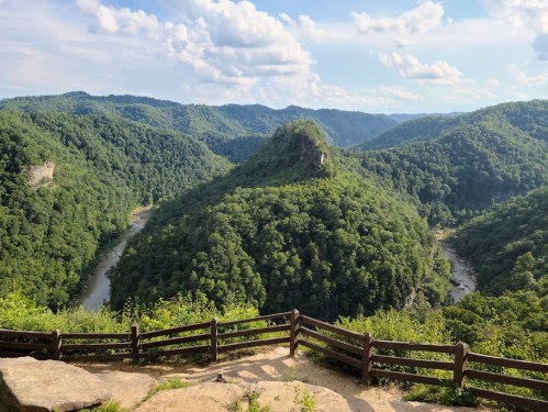 A scenic view of lush green mountains and a winding river under a blue sky with fluffy clouds.