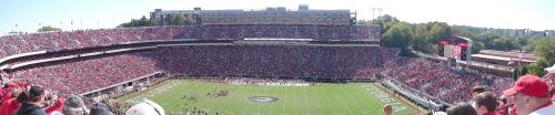 A panoramic view of a packed football stadium with fans in red, showcasing the field and surrounding stands.