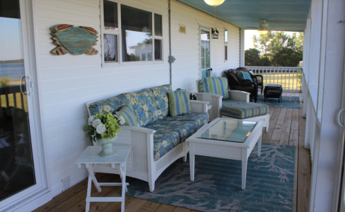 Cozy porch with floral furniture, a glass table, and a view of the water, decorated with a crab motif.