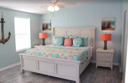 Cozy beach-themed bedroom with a white bed, colorful bedding, orange lamps, and nautical decor.