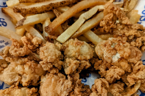 A close-up of crispy fried chicken pieces served with golden French fries on a paper-lined tray.