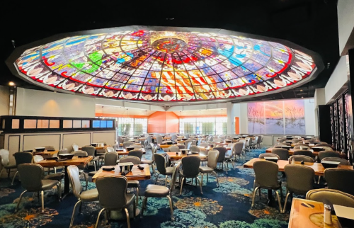 A spacious restaurant interior featuring a colorful stained glass ceiling and neatly arranged tables.
