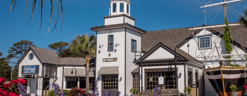 A charming coastal building with a lighthouse tower, surrounded by colorful flowers and a ship display.