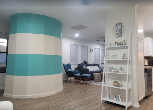 A modern living space featuring a striped turquoise wall, cozy seating area, and a decorative shelf with beach-themed decor.