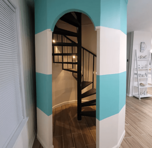 A spiral staircase in a turquoise and white striped alcove, leading to an upper level. Soft lighting illuminates the stairs.