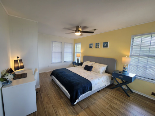 Bright bedroom with a queen bed, yellow walls, two windows, a desk, and modern lamps. Cozy and inviting atmosphere.