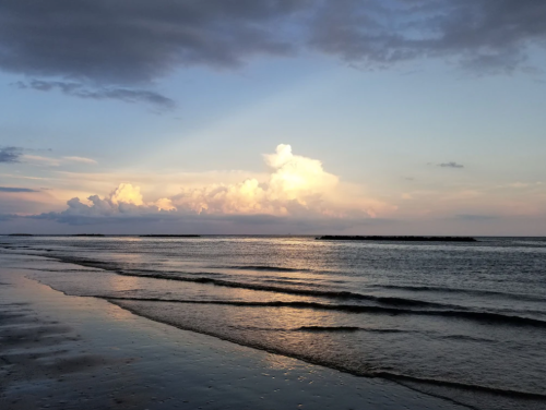 A serene beach at sunset, with gentle waves and colorful clouds reflecting on the water's surface.