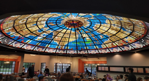 Stained glass ceiling depicting a colorful world map in a restaurant setting with diners below.
