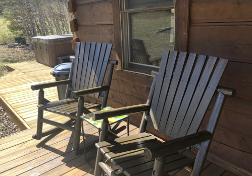 Two wooden rocking chairs on a porch, with a hot tub and a small table in the background.